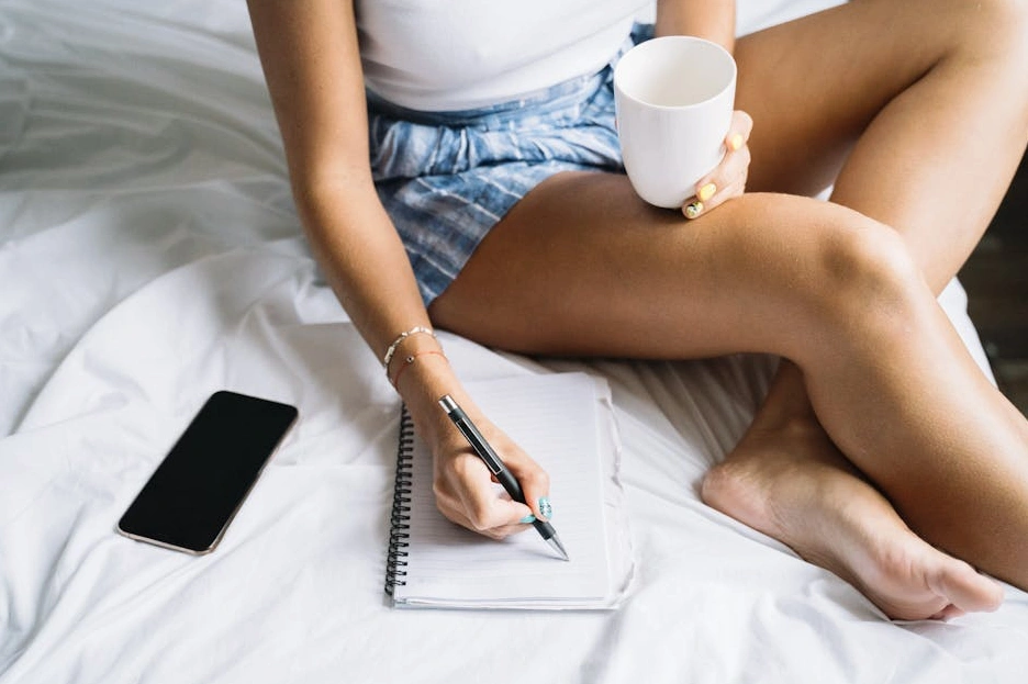 Una persona che scrive su un taccuino con una tazza di caffè accanto.